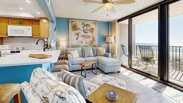 A modern living room with a sofa, a coffee table, and a view of the ocean through large windows. - Sea Colony Ocean beachfront condo with 12 pools, sauna, tennis, private beach (Bethany Beach)