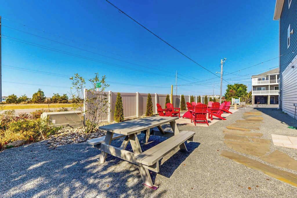 Une terrasse avec une table de pique-nique et des chaises rouges, un chemin de gravier et un bâtiment en arrière-plan.