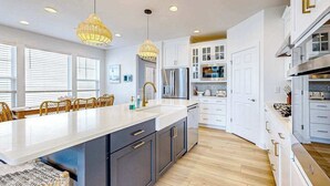 Une cuisine moderne dotée d’un grand îlot central, de luminaires suspendus et de meubles de cuisine blancs.