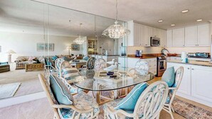 A modern kitchen with white cabinets, a dining area with a glass table and wicker chairs, and a living room with a sofa and a rug. - Kings Grant Beachfront Townhouse w/Ocean Views, Shared Pool, Free WiFi, Private (Fenwick Island)