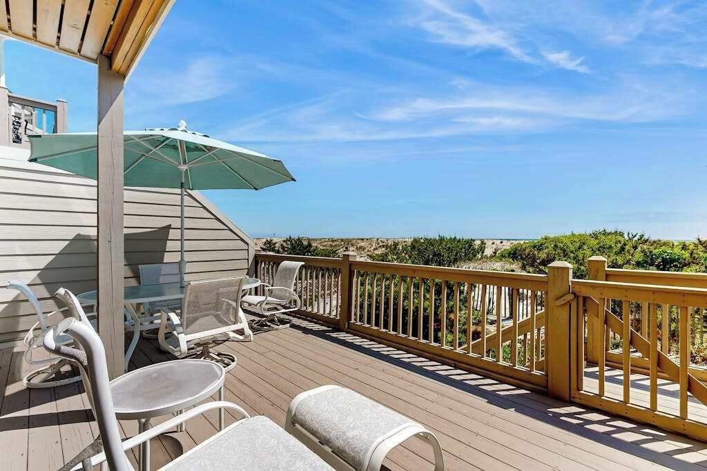 Une terrasse en bois avec des meubles d’extérieur, un parasol vert et une vue sur l’océan.