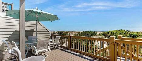 A wooden deck with outdoor furniture, a green umbrella, and a view of the ocean.
