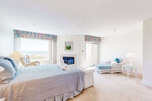 Ein Schlafzimmer mit einem Bett, zwei Stühlen, einem kleinen Tisch, einem Kamin und großen Fenstern.
