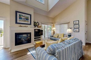 A living room with a fireplace, a sofa set, a television, and framed pictures on the wall. - Sea Colony Tennis condo w/ basketball court, gym, pool & tennis courts (Bethany Beach)