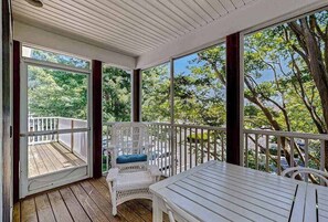 A covered porch with a white chair and table, large windows, and a view of trees. - Sea Colony Tennis condo w/ basketball court, gym, pool & tennis courts (Bethany Beach)