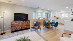 Un salon moderne doté d’un téléviseur à écran plat, d’un meuble de rangement en bois et d’un coin repas avec des chaises bleues.