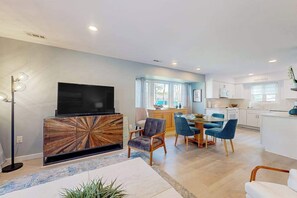 A modern living room with a flat-screen TV, a wooden entertainment unit, and a dining area with blue chairs. - Sea Colony condo with 12 pools, private beach, tennis, shuttle, gym, & deck (Bethany Beach)