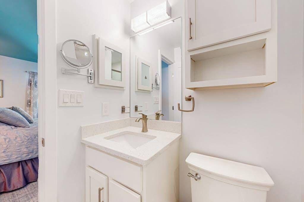 Une salle de bain avec un lavabo blanc, un miroir, des toilettes et une étagère.