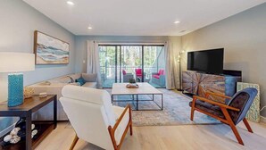 Un salon moderne avec un canapé, une table basse, un téléviseur et une vue dégagée grâce à de grandes portes vitrées.