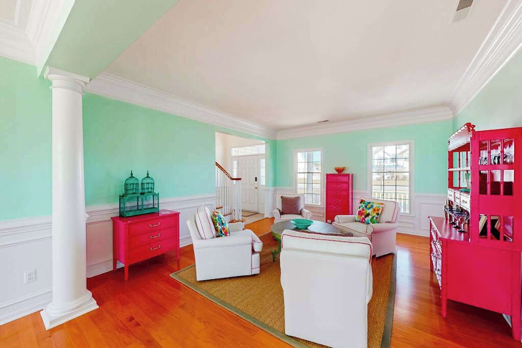 Un salon spacieux avec un escalier, des meubles blancs et roses, et une grande fenêtre.