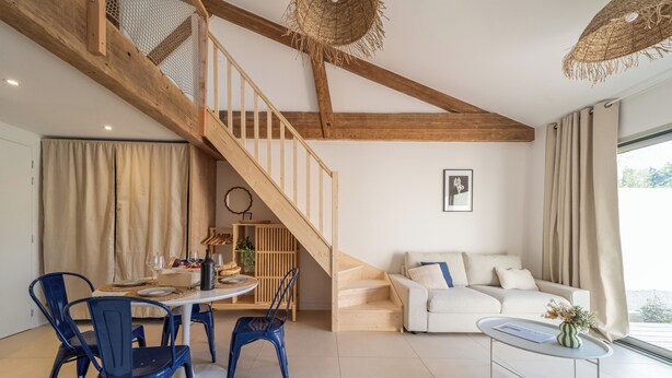 Een moderne woonkamer met een trap, een eethoek met blauwe stoelen, een witte bank en een salontafel.