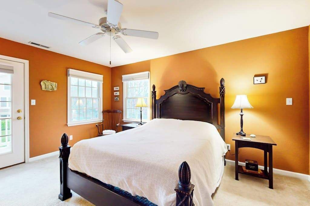 A bedroom with a bed, a ceiling fan, a nightstand, a lamp, and a window.