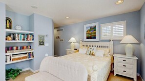 A bedroom with a bed, bedside tables, a bookshelf, and a window with blinds. - Updated Waterside home near beach with screened deck & community pool (Frankford)