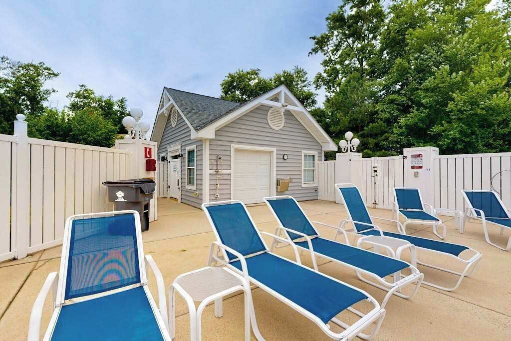 A poolside area with lounge chairs, a small building with a garage, and a white fence.