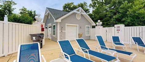 A poolside area with lounge chairs, a small building with a garage, and a white fence.