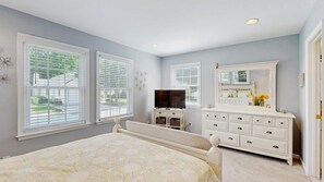 A bedroom with a bed, dresser, television, and large windows. - Updated Waterside home near beach with screened deck & community pool (Frankford)