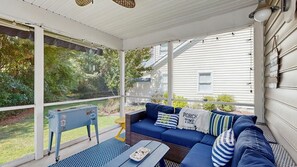 En inglasad veranda med en blå soffa, kuddar och ett litet bord.