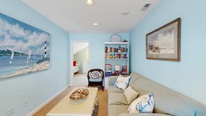 A living room with a sofa, coffee table, bookshelf, and two paintings. - Updated Waterside home near beach with screened deck & community pool (Frankford)