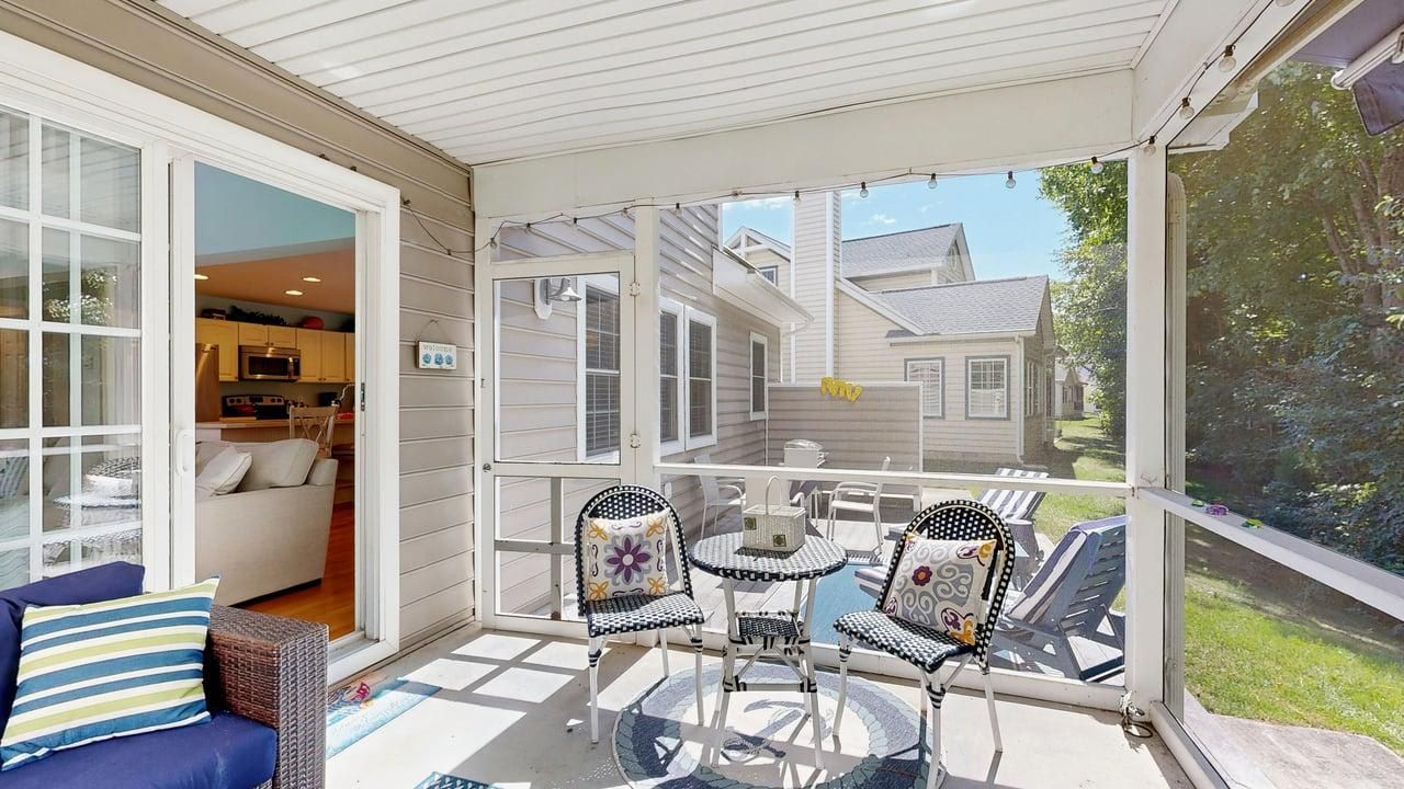 A covered patio with a dining table and chairs, a sofa, and a view of a house and garden.