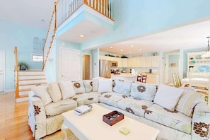 A spacious living room with a large sectional sofa, a dining area, and a kitchen in the background. - Updated Waterside home near beach with screened deck & community pool (Frankford)