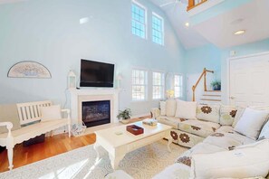 A living room with a fireplace, white furniture, a television, and a staircase. - Updated Waterside home near beach with screened deck & community pool (Frankford)