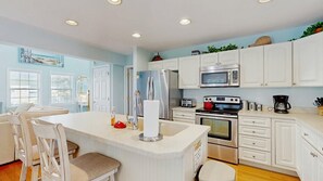 A modern kitchen with white cabinets, stainless steel appliances, and a central island with seating. - Updated Waterside home near beach with screened deck & community pool (Frankford)