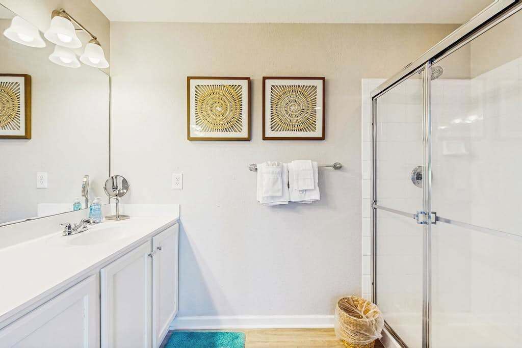 A bathroom with a white vanity, a mirror, a shower with a glass door, and two framed wall art pieces.