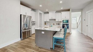 A modern kitchen with white cabinetry, a stainless steel refrigerator, and a central island with a sink. - Stingray Harbor condo with W/D, WIFI, close to restaurants (Ocean View)