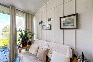 Una sala de estar con un sofá, una mesa con plantas, un cuadro enmarcado y una ventana con cortinas.
