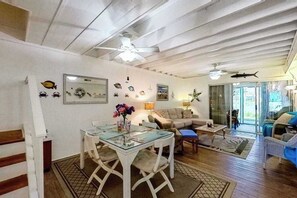 Una sala de estar con una mesa de vidrio, un sofá, un ventilador de techo y decoraciones en la pared.