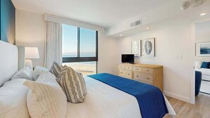 Une chambre d’hôtel avec un grand lit, une télévision, une commode et une vue sur la plage.