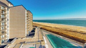 Un immeuble de grande hauteur doté de nombreux balcons donnant sur une plage et l’océan.