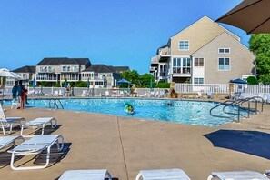 A swimming pool area with lounge chairs, a poolside fence, and residential buildings in the background. - Bayville Shores townhome, AC, & W/D - pool, gym & tennis court access (Selbyville)