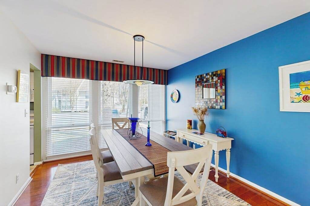 Uma sala de jantar com mesa de madeira, cadeiras brancas, parede azul e janela com persianas.