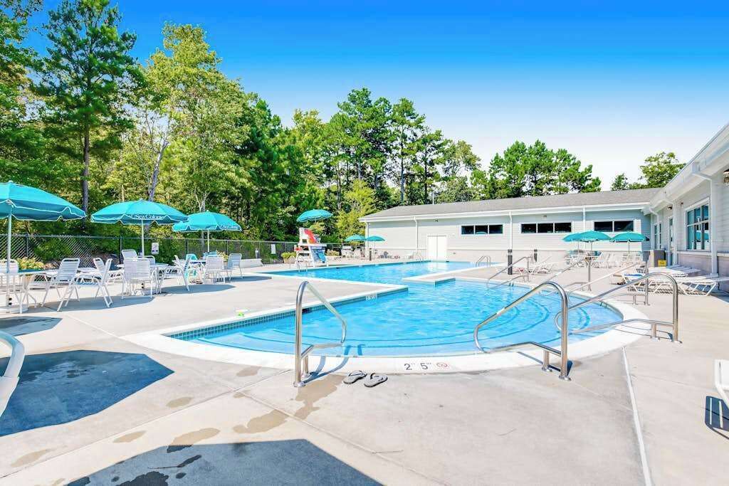 Ein Schwimmbecken mit Liegestühlen und Sonnenschirmen, umgeben von Bäumen.