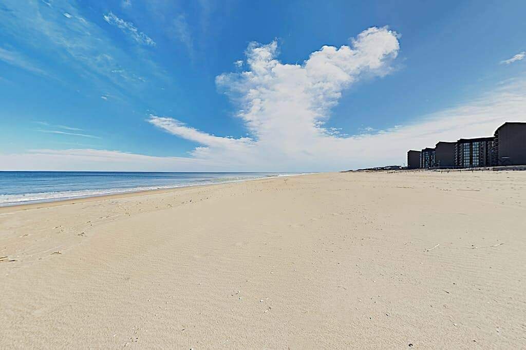 A beach with a clear sky, a sandy shore, and a building with multiple floors.