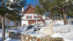 A chalet with a stone wall and a large planter in a snowy landscape.