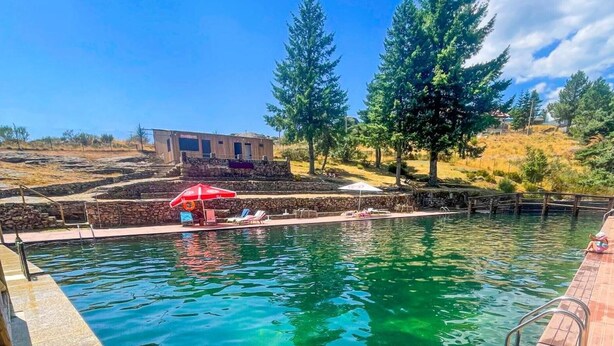 A swimming pool with clear water, a wooden deck, and a red umbrella.