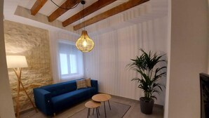 A living room with a blue sofa, a small round table, a hanging light fixture, a floor lamp, and a potted plant. - Deluxe Compact Flat With Jacuzzi (Alicante)