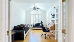Ein Zimmer mit Deckenventilator, Klavier, Sofa und einem Fenster mit Jalousien.