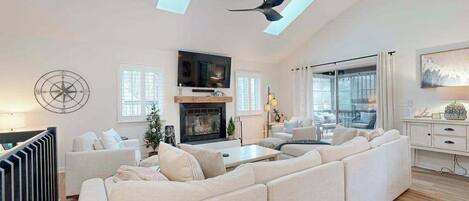 A spacious living room with a fireplace, a large sofa, a TV, and a ceiling fan.