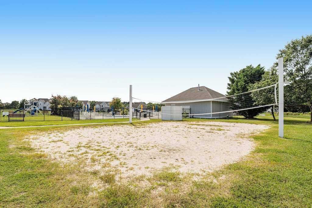 Una cancha de voleibol con red, rodeada de césped y un edificio al fondo.