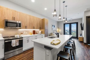 A modern kitchen with wooden cabinets, stainless steel appliances, and a central island with stools. - 12 Min to Downtown Pool Balcony Free Parking (Austin)
