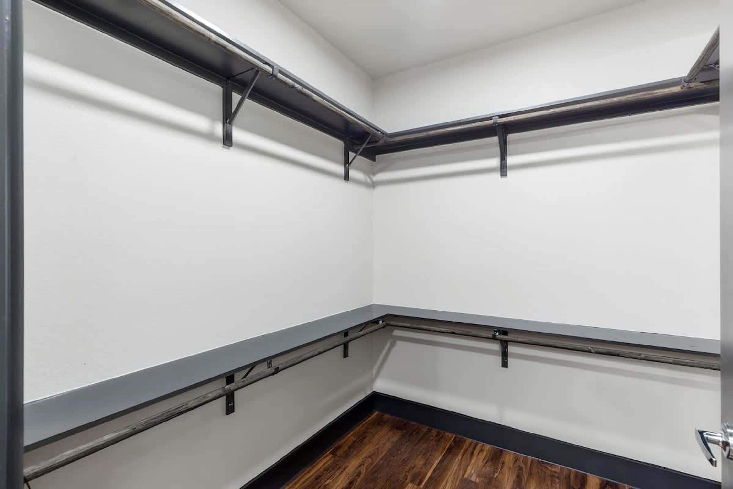 Rincón de una habitación con paredes blancas, suelo oscuro y vigas de metal negro.