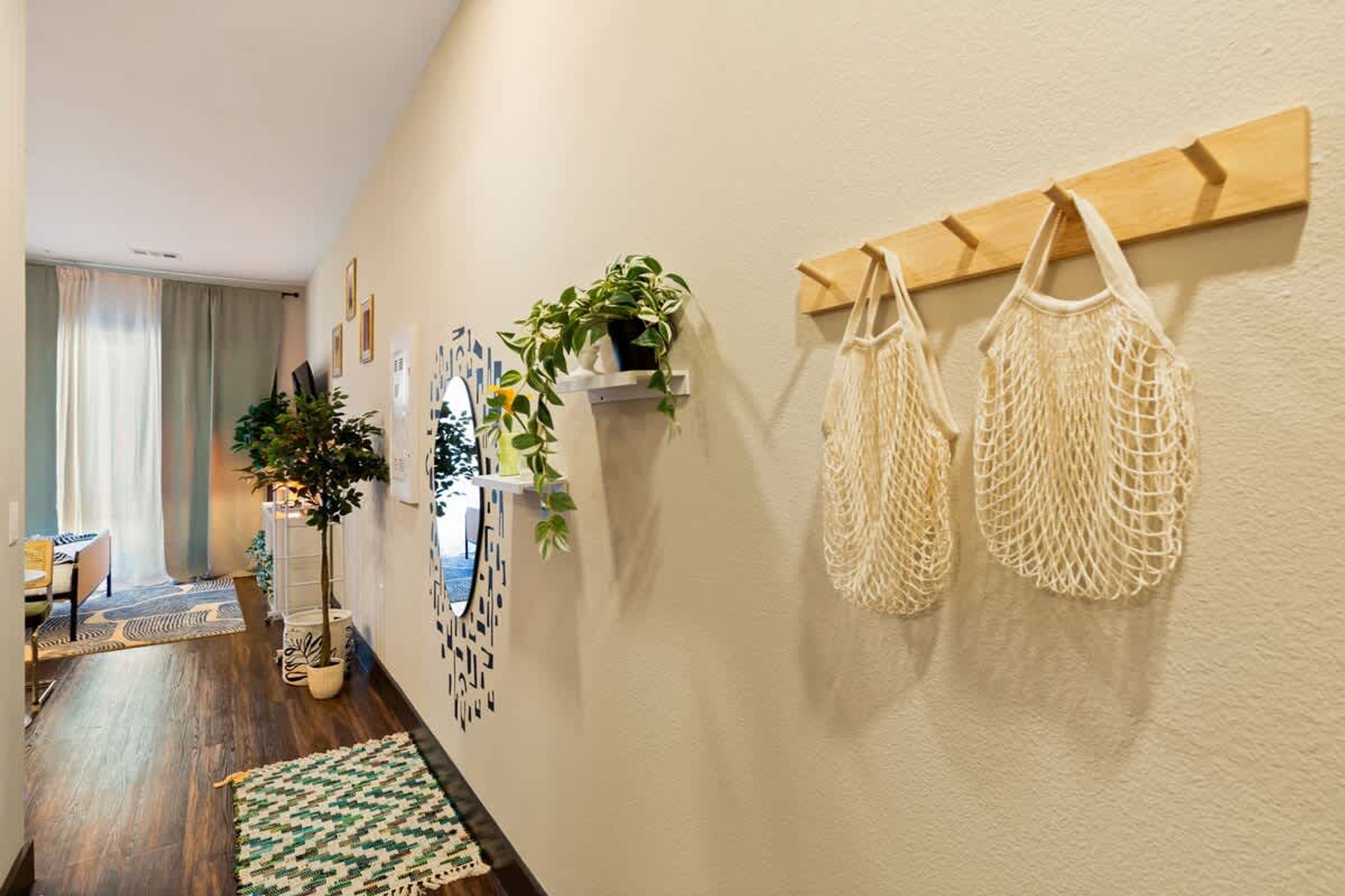 Un pasillo con piso de madera, un tapete de diseño verde y blanco, una planta en un estante y dos adornos de macramé en la pared.