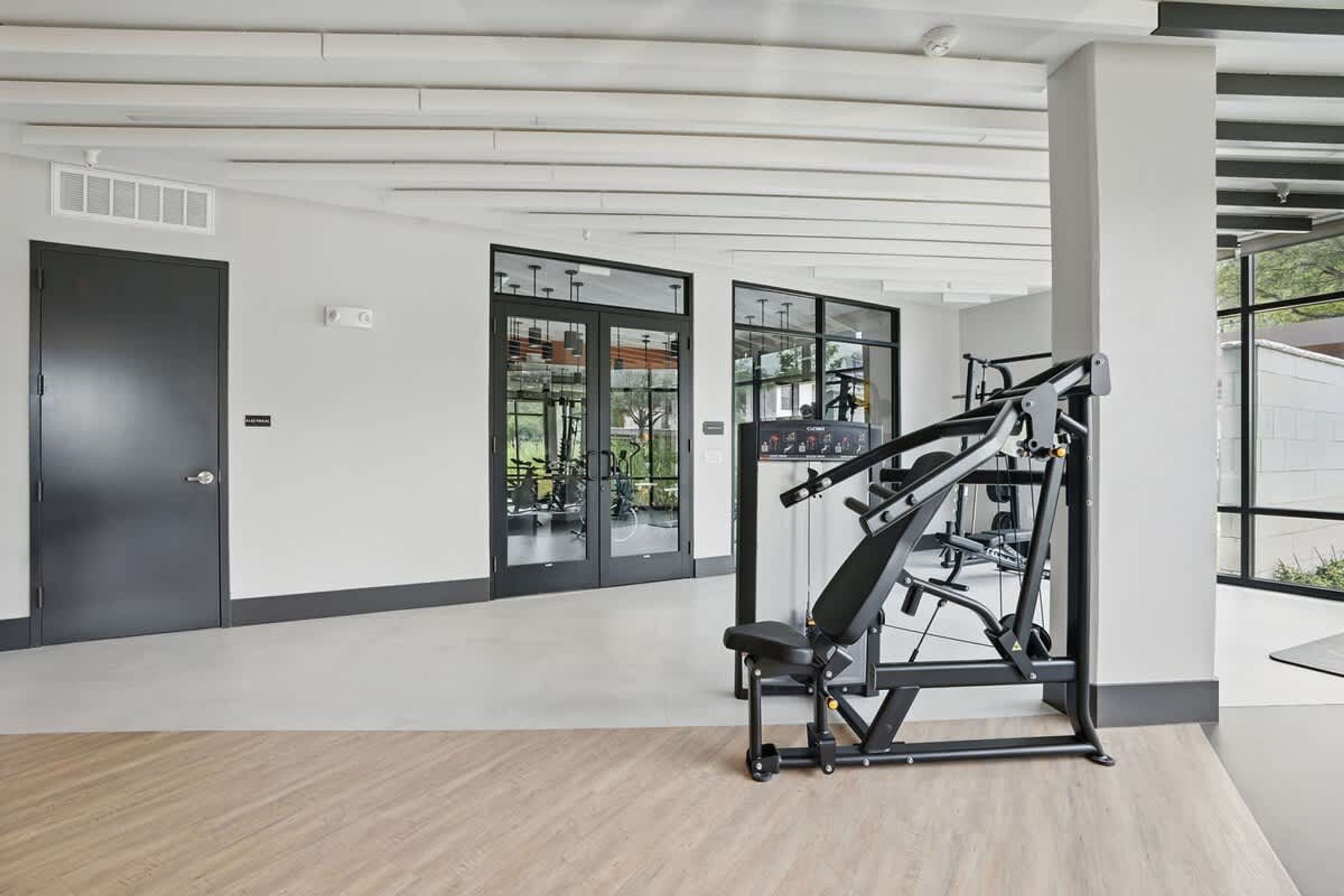 Un gimnasio con equipo de ejercicio, una puerta y ventanas amplias.