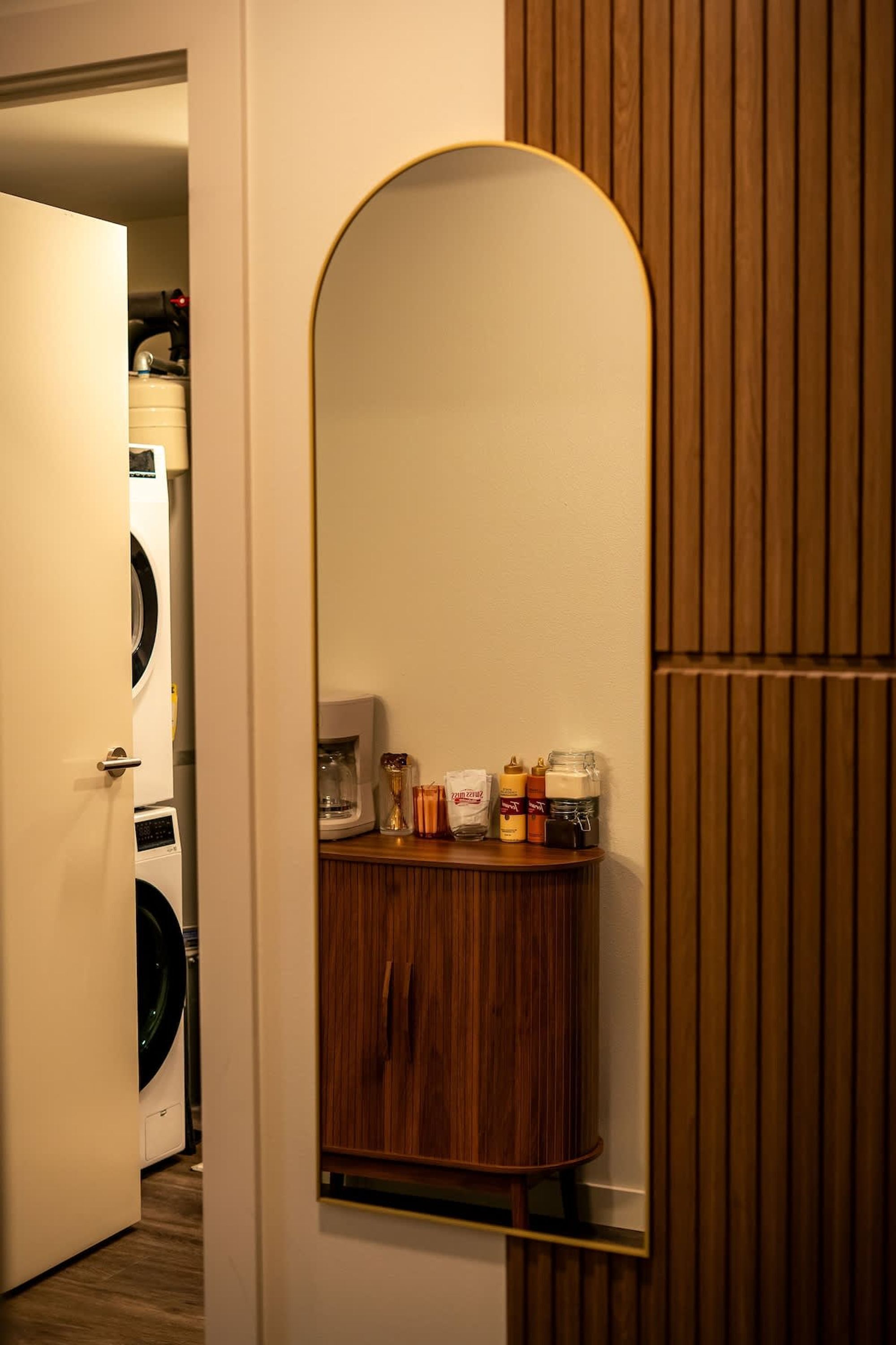 Una habitación con un armario de madera, un espejo y una cafetera sobre una encimera.