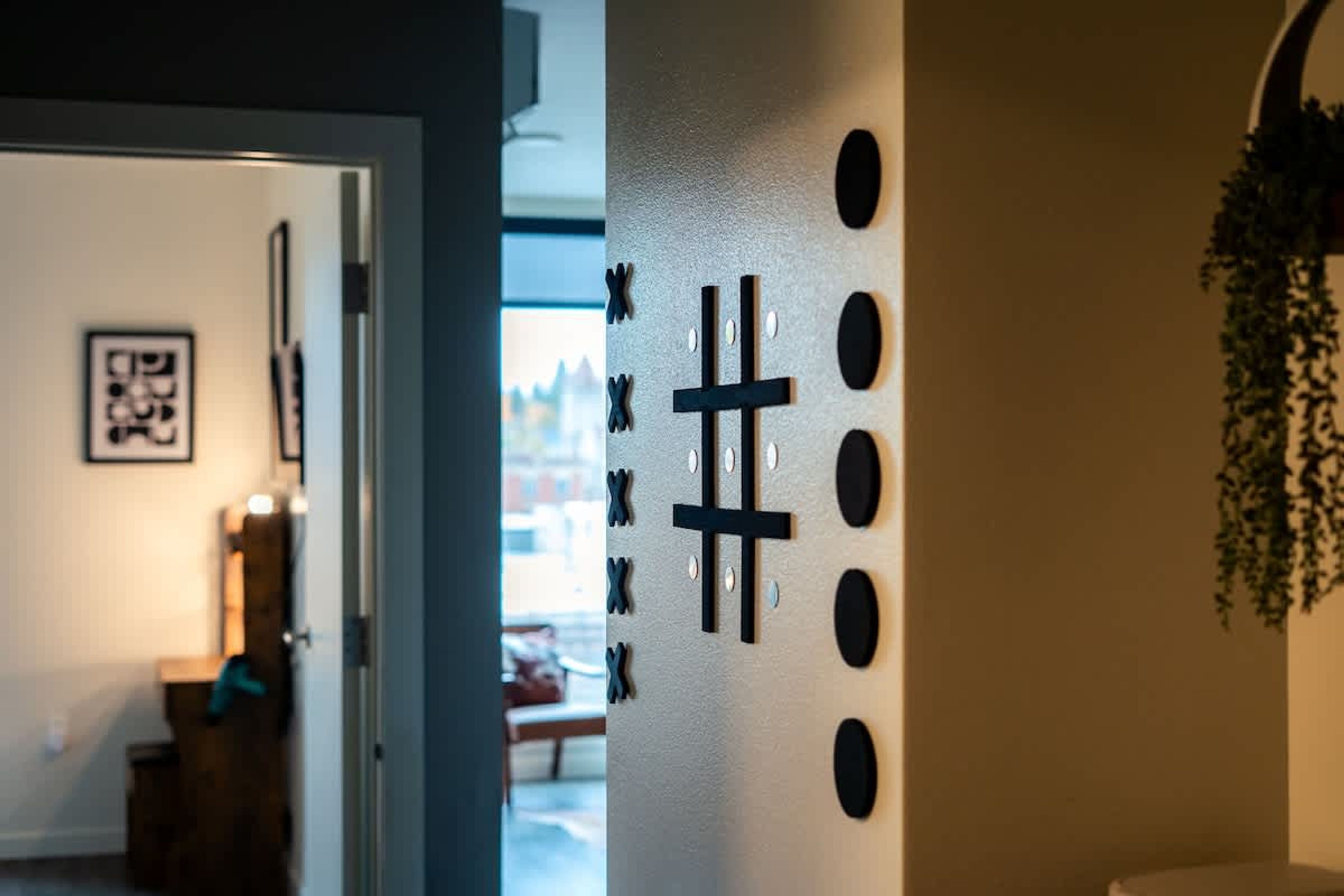 Un pasillo con un diseño mural que incluye una cruz y círculos, una puerta que da a otra habitación y una planta colgante.