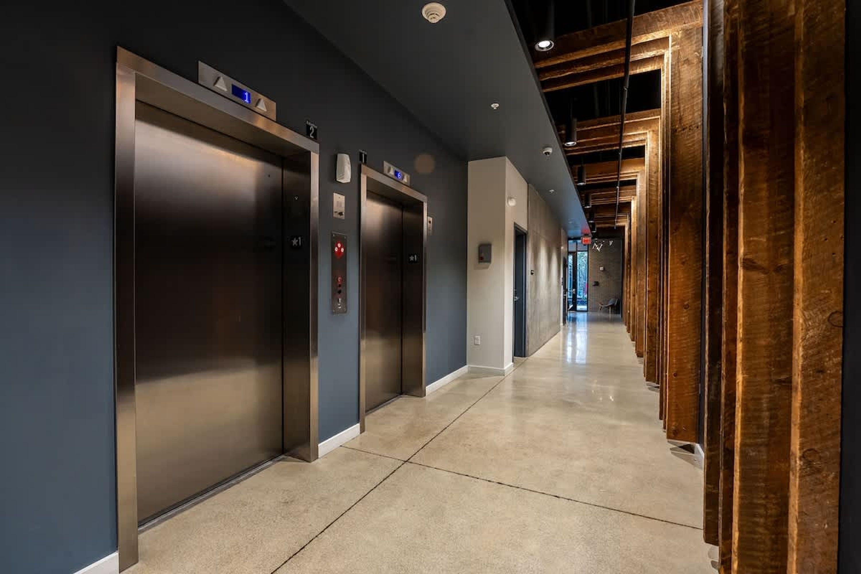 A modern hallway with three elevators, a polished floor, and wooden paneling on the right.