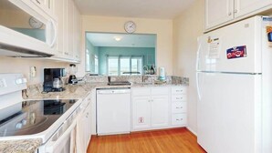 A kitchen with white cabinets, a dishwasher, a refrigerator, and a clock on the wall. - Charming condo with nearby golf, outdoor pool & close to the beach (Ocean View)